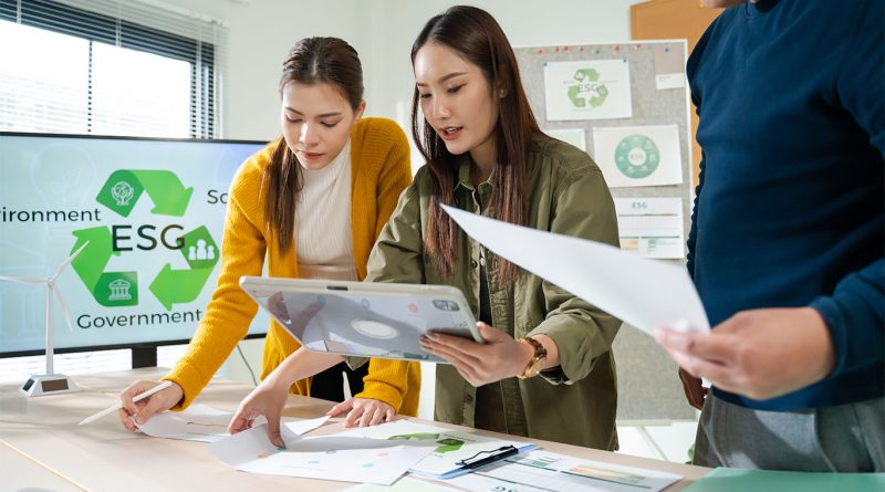 Three professionals collaborating on ESG and sustainability reports in an office with charts and infographics on net zero and environmental strategy.