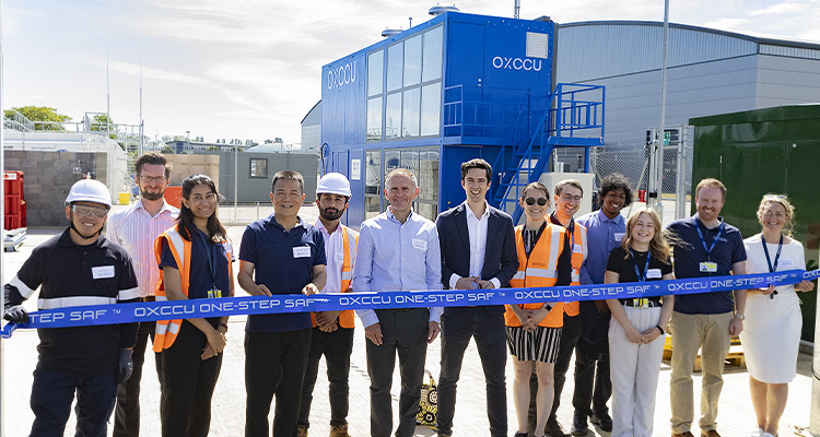 a group of people from the company OXCCU posing for a photo in front of a blue industrial plant