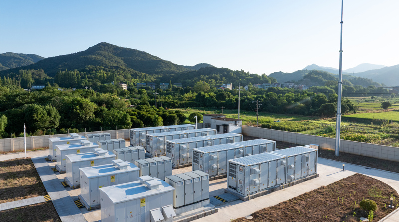 A large-scale battery energy storage facility set against a green landscape with hills and power infrastructure in the background, representing advanced grid solutions in 2026.
